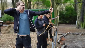 Bogen schießend, vier Personen im Wald, zielend auf Zielscheiben.