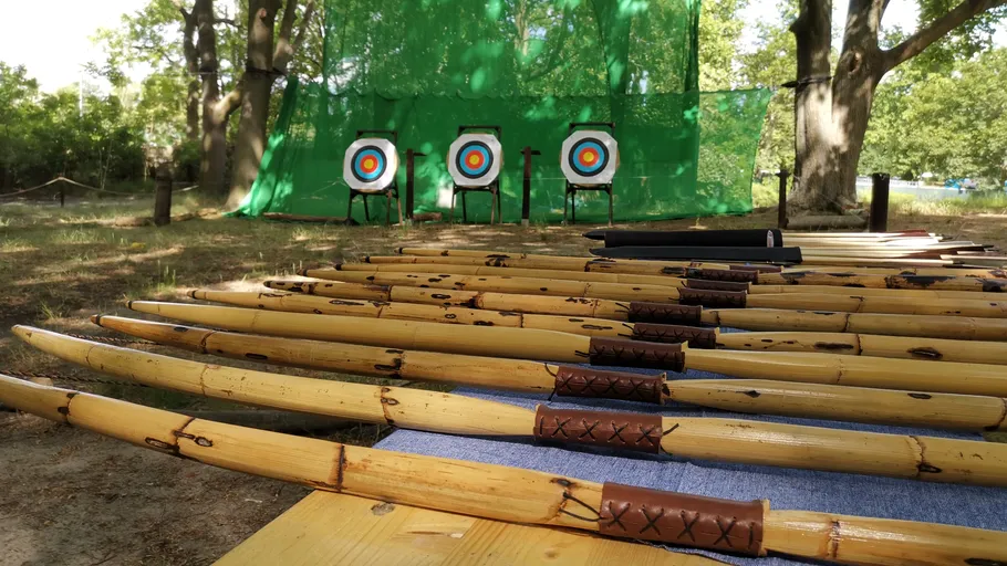 Bows and arrows lie in front of outdoor targets.
