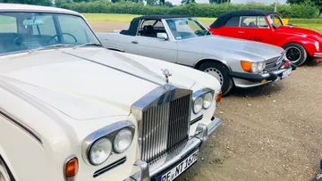 Three cars are parked on a gravel field in nature.