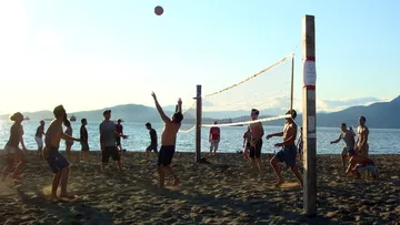 People play beach volleyball on the beach with water in the background.