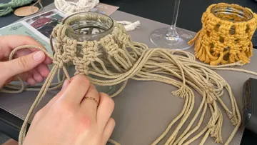 Hands tie string around a glass in a creative space.