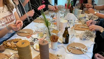 Tisch mit Bastelmaterialien und Menschen, die schnüren.