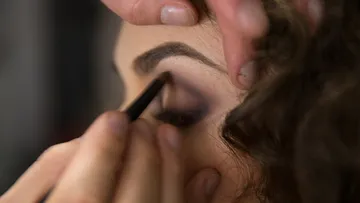 Eine Person schminkt das Augenlid einer anderen Person.