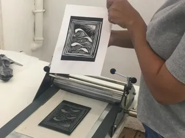 Drucker holds printed sheets over a printing press in the workshop.
