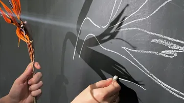 Hands drawing a flower shadow on chalkboard.