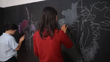 Two people drawing flowers on chalkboard.
