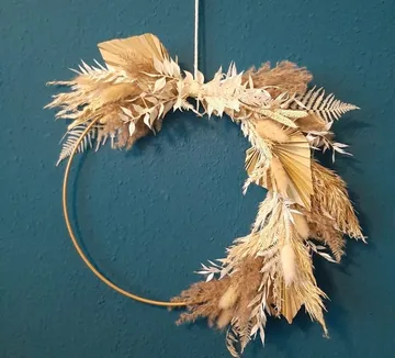 Circular wreath of dried flowers hangs on a blue wall.