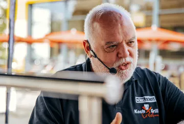 Man talking with headset, umbrellas visible in the background.