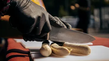 Person schneidet Gemüse mit einem Messer auf einem Tisch.