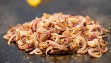 Gebratene Zwiebeln liegen auf einer heißen Grillfläche.