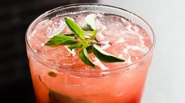 A glass of pink cocktail and fresh herbs.
