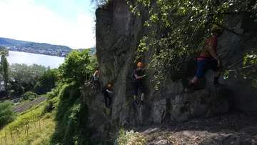 Five people climb along a rock wall surrounded by nature.