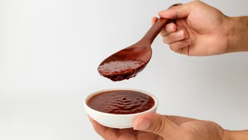 Holzlöffel hebt scharfe Soße über einer kleinen Schüssel.