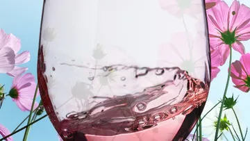 Ein Glas gefüllt mit Roséwein steht zwischen Blumen.