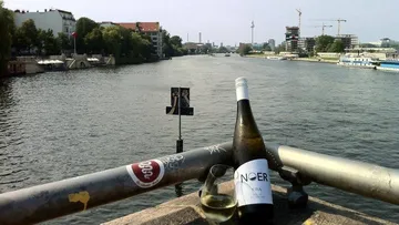 Weinflasche steht am Geländer entlang eines Flusses mit Gebäuden.