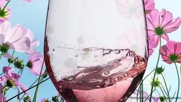 Glas mit rosafarbenem Getränk unter bunten Blumen, mit Himmel.