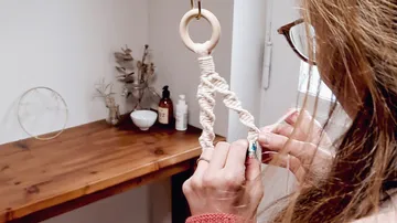 Eine Person knotet dekorative Schnüre an einem Holzring.
