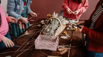 Hände gestalten Blumenkränze auf einem Tisch aus Holz.
