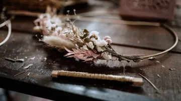 Blumenkranz liegt auf einem Tisch, umgeben von Bastelmaterialien.