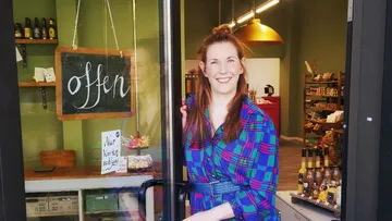 Shop opens, smiling woman stands in the entrance.