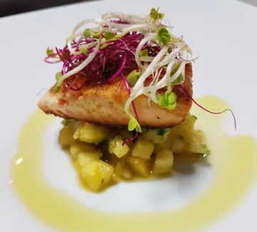 Fried piece of fish is placed on pineapple salad, decorated with herbs.