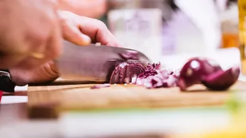 Onion is cut into pieces on a wooden board.