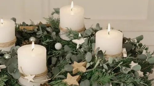 Weiße Kerzen stehen auf einem Adventskranz aus Tannenzweigen.