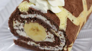 Bananen-Rolle mit Sahne auf einem transparenten Teller.