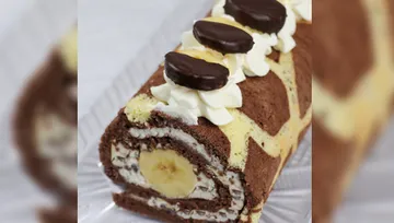 Schokoladen-Biskuitrolle mit Bananenfüllung und Sahne-Dekoration.