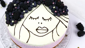 Kuchen mit Gesicht und Beeren als Dekoration auf Glasplatte.