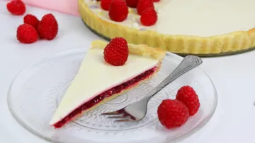 Cake piece has raspberry filling and cream topping, decorated with raspberries.
