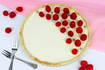Cake decorated with raspberries, on table with towel.