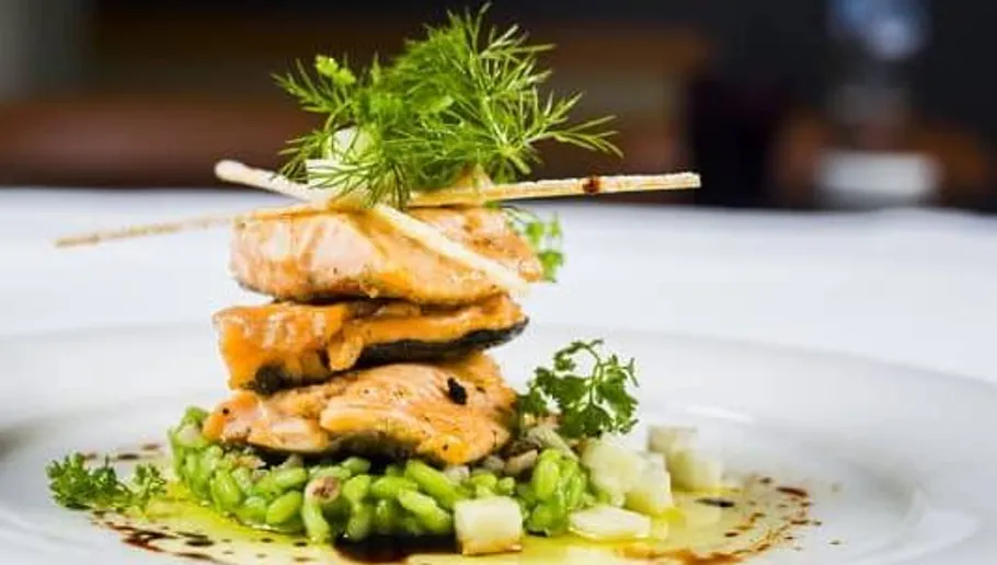 Salmon on green risotto, decorated with herbs.