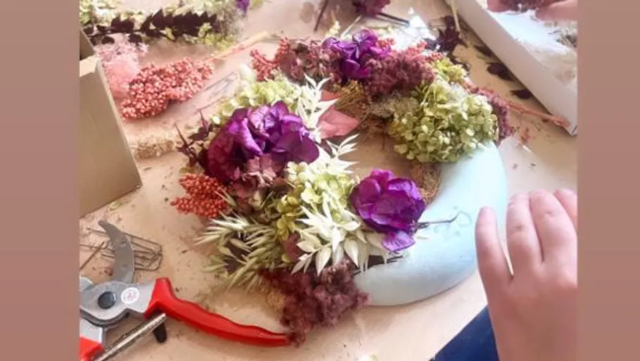 Flower wreath is created on a table using tools.