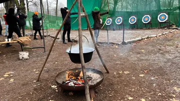 Pendelleuchte über Feuer, während Teilnehmer im Freien Bogenschießen.
