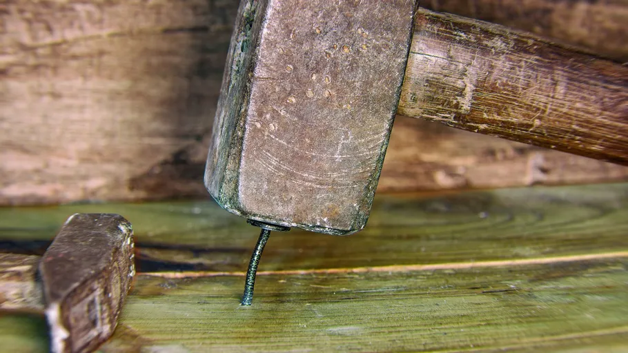 A hammer hits a nail on a wooden surface.