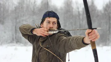 Mann schießt mit Pfeil und Bogen im Schnee.