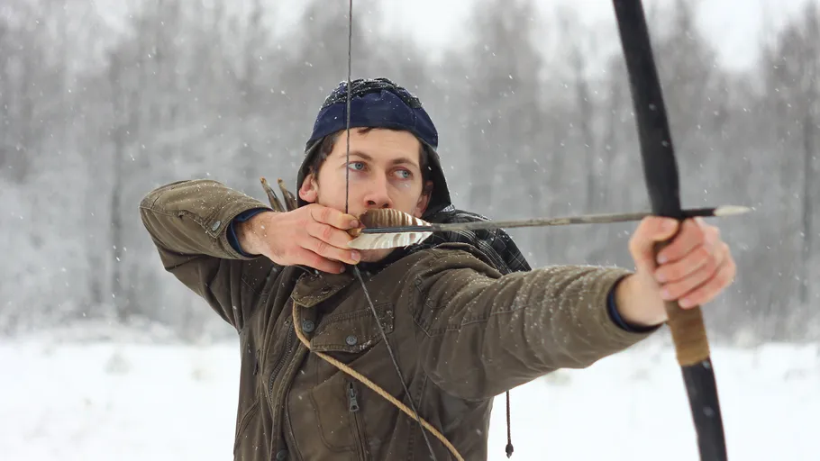 Man shoots with a bow and arrow in the snow.