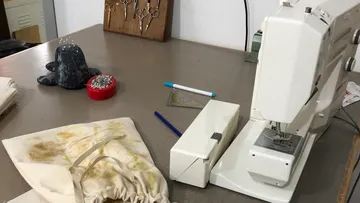 Nähmaschine auf einem Tisch, umgeben von Stoffen und Werkzeugen.