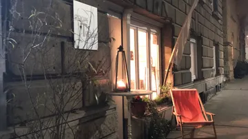 Ein Stuhl steht neben einem beleuchteten Fenster, nachts.