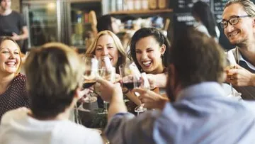 Six people toast with glasses in a restaurant.