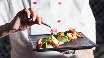 Cook uses tweezers to decorate an artistic dish.
