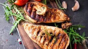 Gegrillte Hähnchenbrust auf einem Holzbrett mit Gemüse.