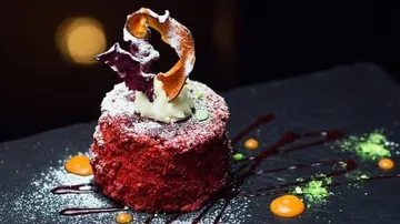 Rote Torte mit Dekoration auf einer dunklen Platte serviert.