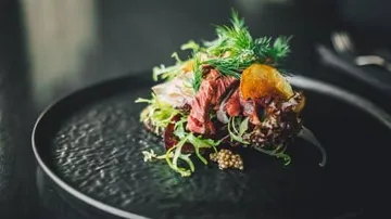 Ein Gericht mit Fleisch, Gemüse und Kräutern auf einem Teller.