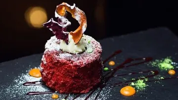 Roter Kuchen mit Sahne auf schwarzem Teller, dekoriert.