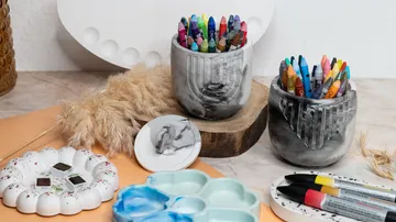 Bunte Stifte stehen in Töpfen auf einem Tisch.