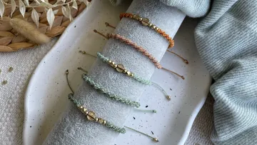 Bunte Armbänder liegen auf einem grauen Kissen.