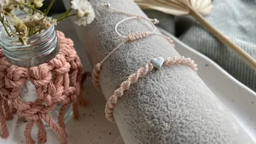 Armband auf einem grauen Handtuch neben einer Blumenvase.