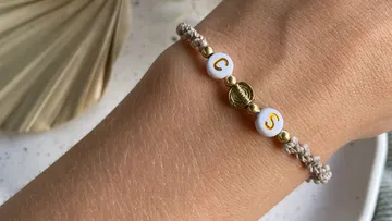 Armband mit Buchstaben und goldenen Perlen an Hand.